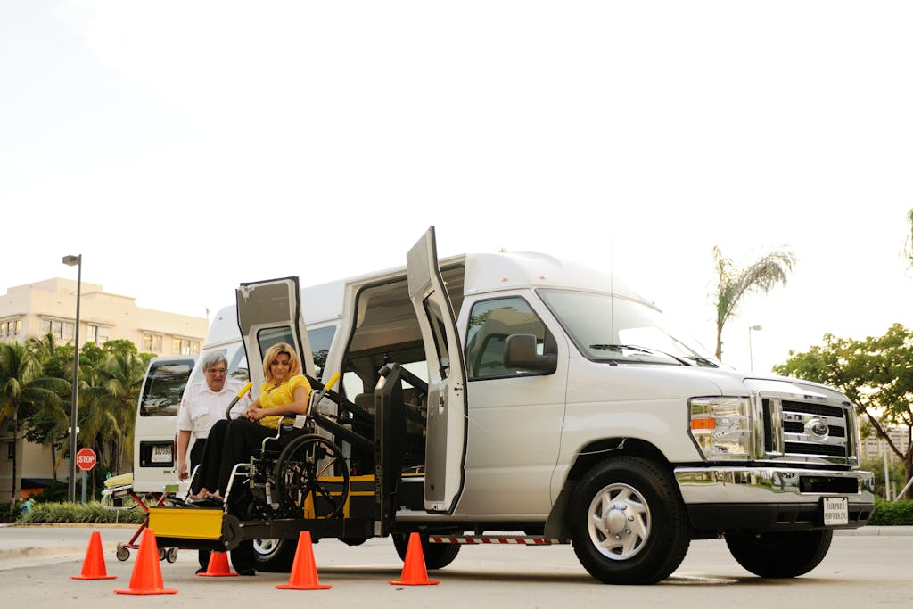 A woman in a wheelchair uses a lift to board an accessibility van assisted by a driver.