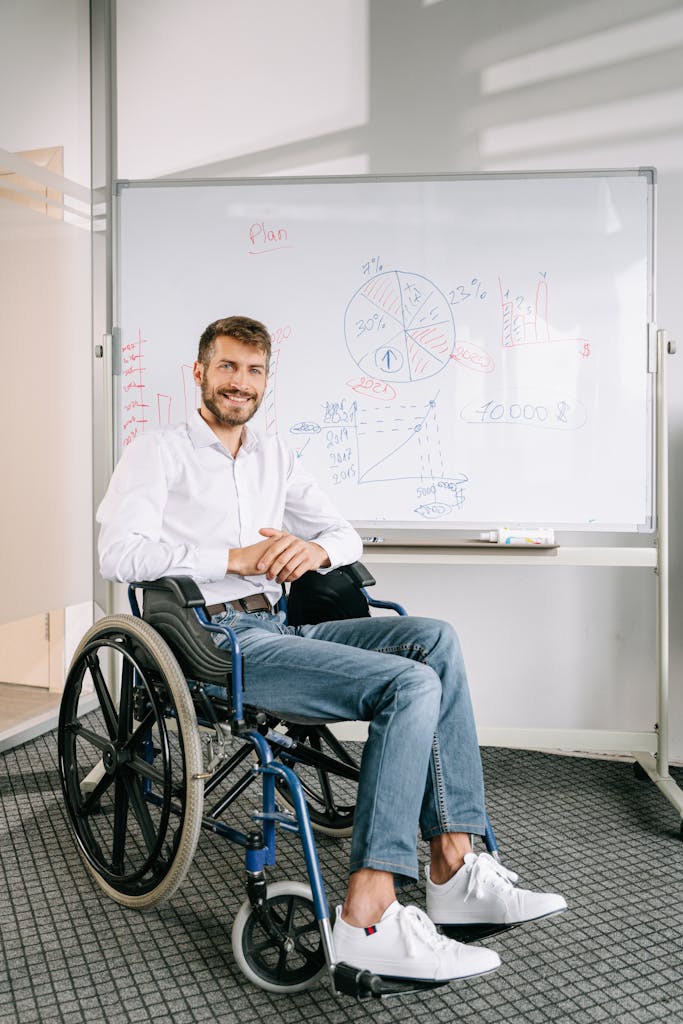 Smiling man in wheelchair presenting data at office whiteboard